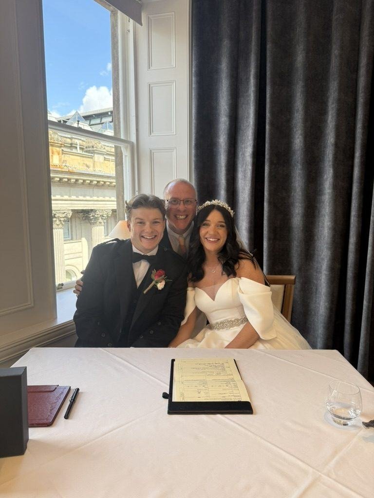 Aimee and Ollie with celebrant John Paul at the signing table at The Exchange, the Marriage Schedule in front of them
