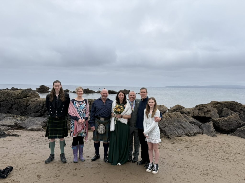 A family gathered for a beach wedding on Arran, rocks and sea behind