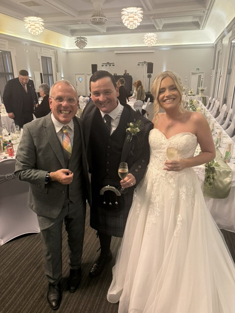 A newly married couple with celebrant John Paul raising a toast in the Saltcoats Town Hall function room, set for the wedding reception