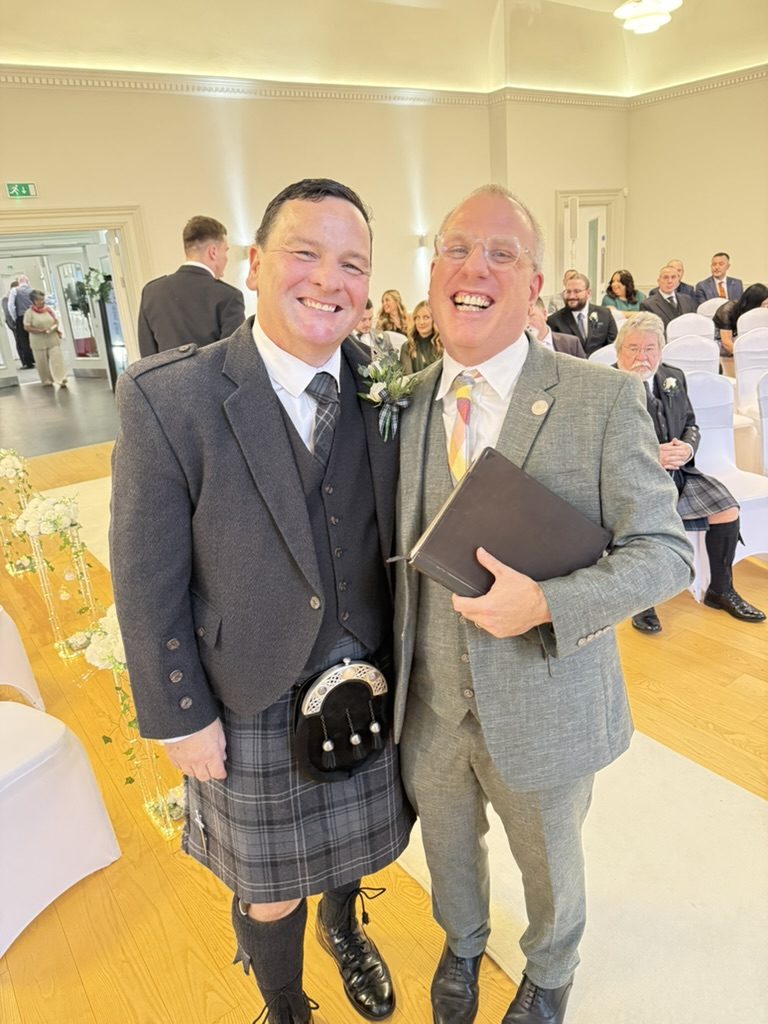 Celebrant John Paul and groom Barry mid-ceremony at Saltcoats Town Hall, with seated guests in the background