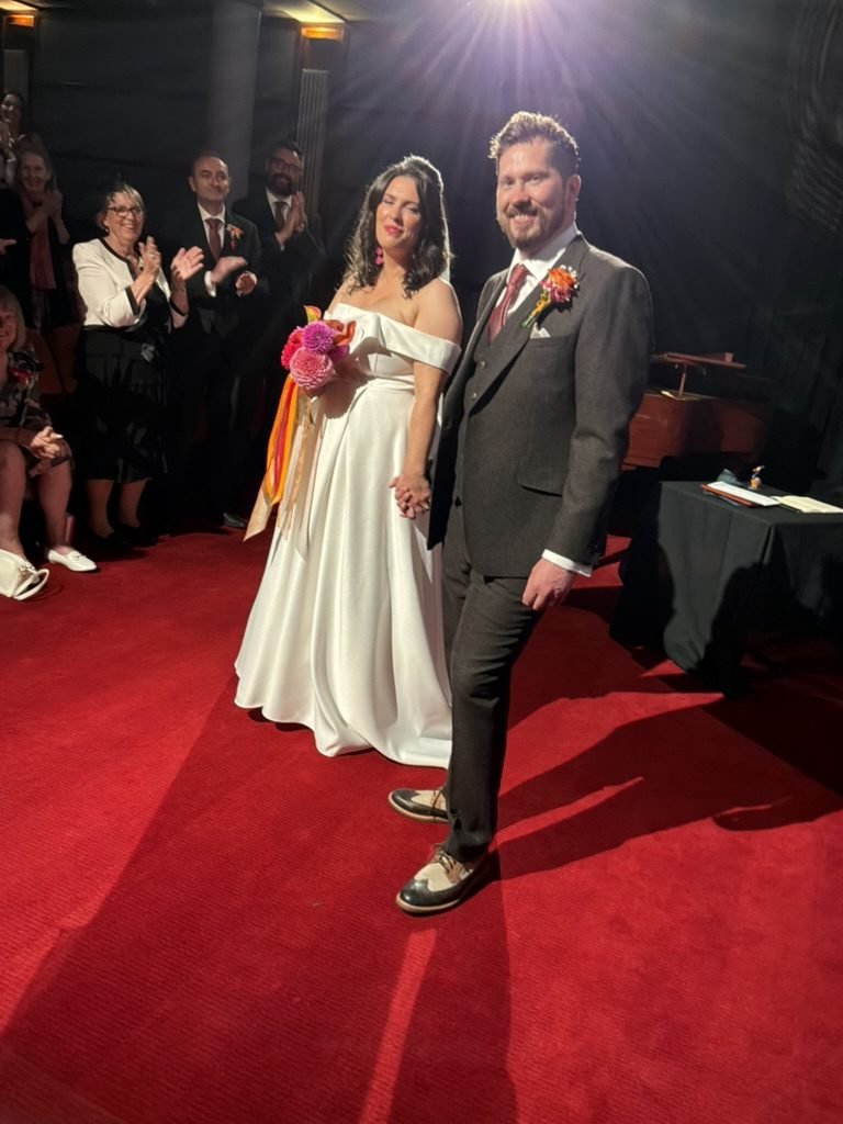 Becky and Tom hand in hand on the red carpet in Cinema 2 of the Glasgow Film Theatre, guests applauding from the cinema seats behind them