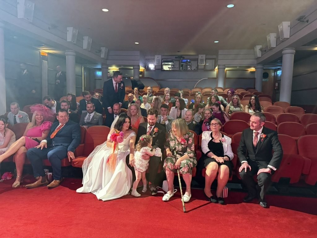 The auditorium of Cinema 2 at the Glasgow Film Theatre filled with wedding guests seated in the red cinema seats, a popcorn box at every place