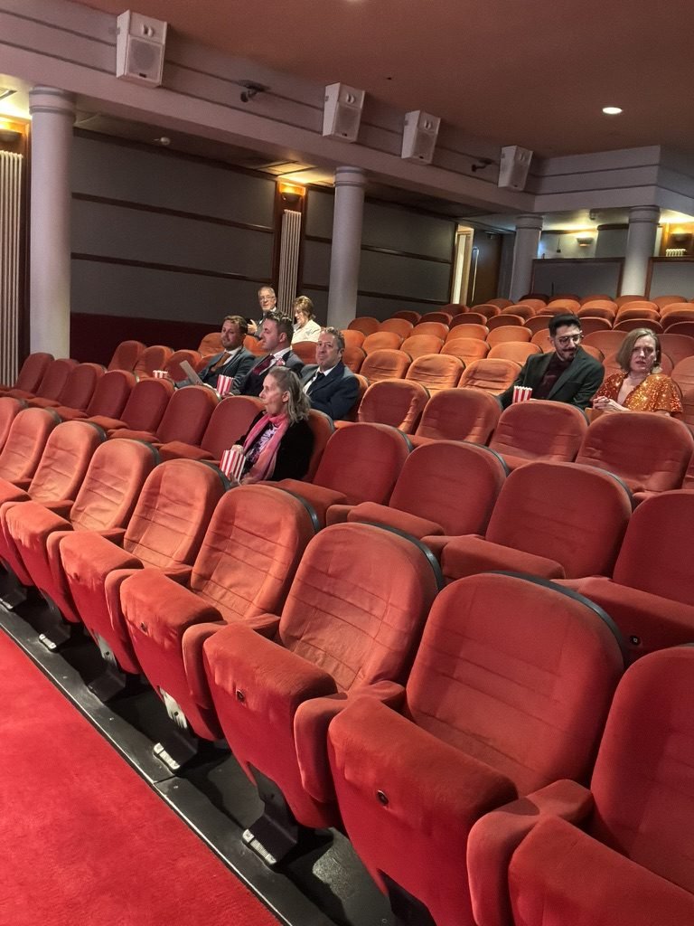 Wedding guests seated in the deep red cinema seats of the Glasgow Film Theatre, each holding a striped popcorn box