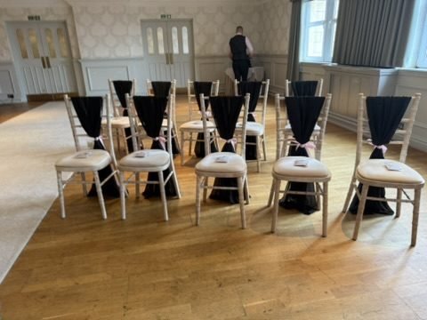 The Fairfield Suite at Fairfield House Hotel set for a ceremony before the guests arrive: rows of pale chairs dressed with black sashes on a wooden floor, panelled walls with patterned wallpaper, double doors and tall windows