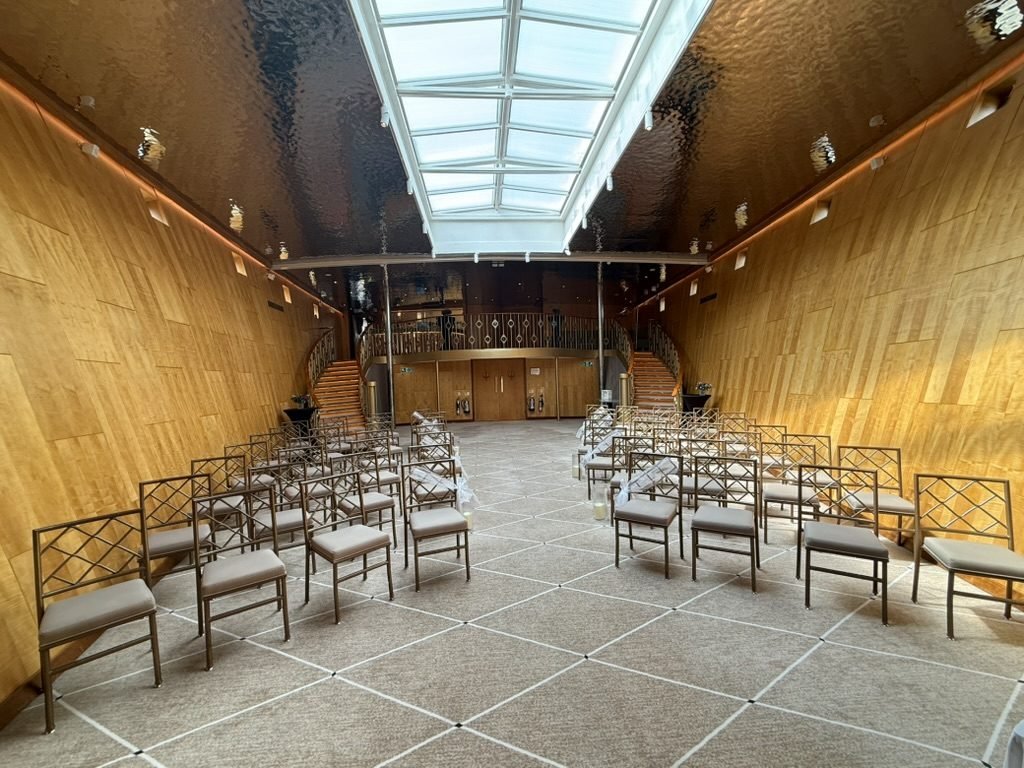 The Ballroom aboard Fingal set for a humanist wedding, rows of chairs either side of an aisle under a long skylight, curved timber walls following the line of the hull and twin staircases rising to a gallery at the far end