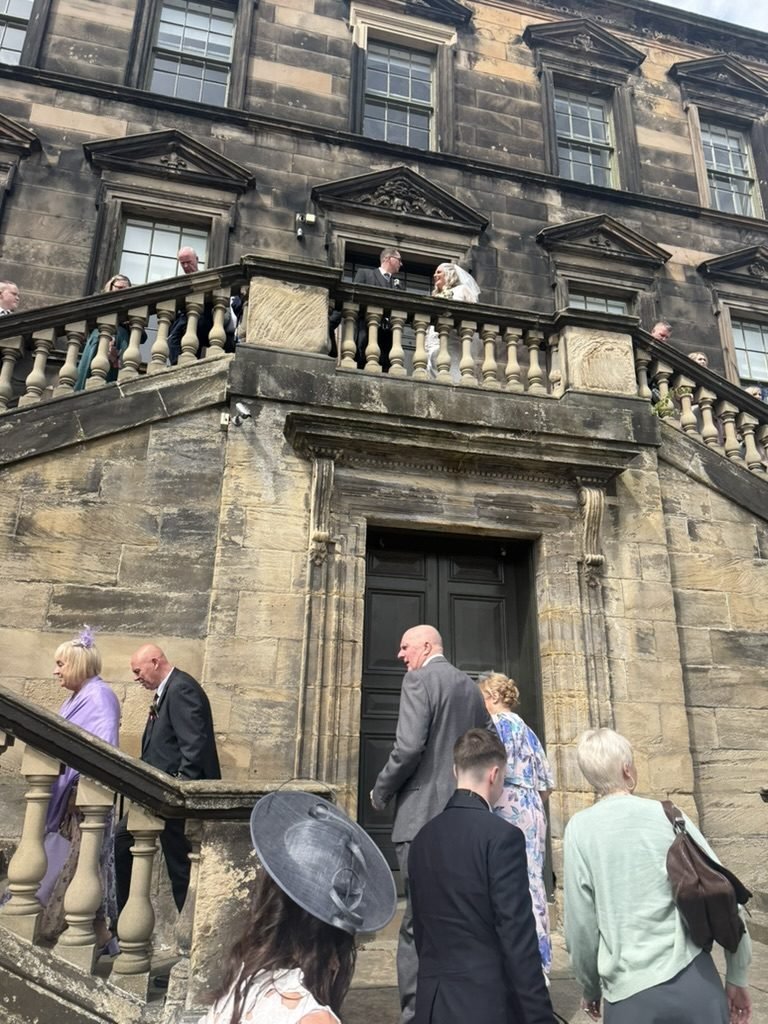 The historic facade of West Lothian Burgh Halls, guests gathered on the steps as the bride and groom appear on the balcony above