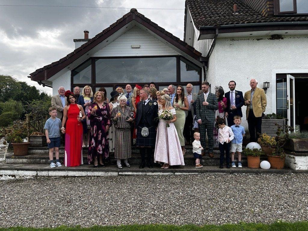 Christine and Stewart's wedding party gathered on the steps of the white farmhouse at Fruin Farm, Glen Fruin