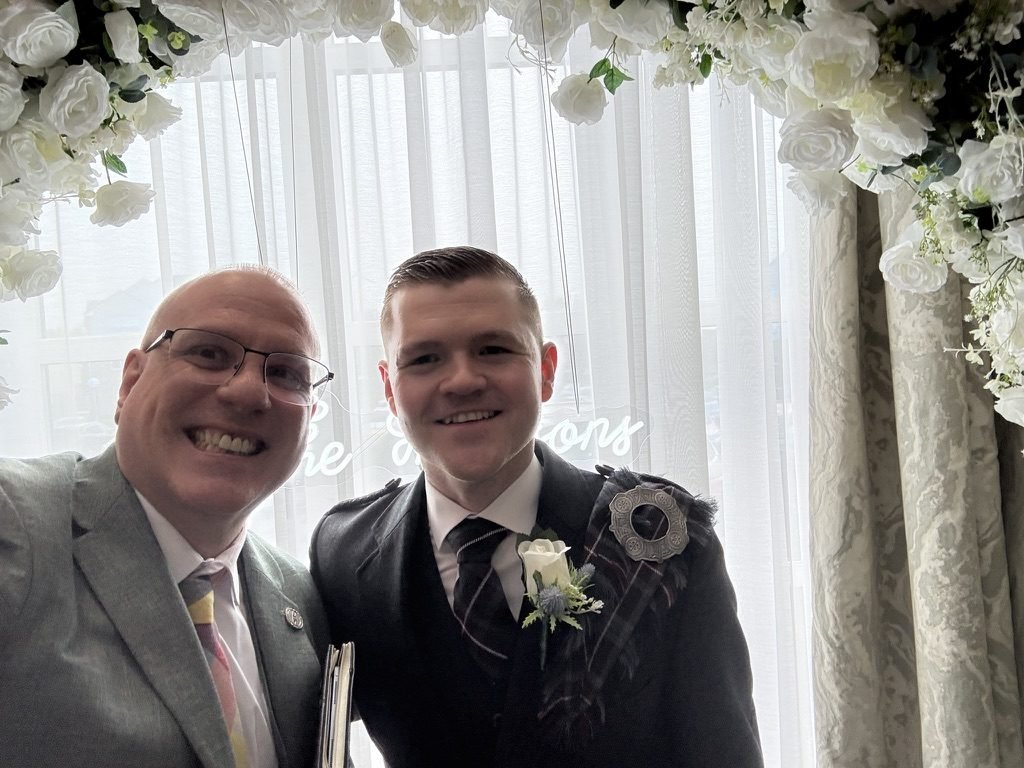 Celebrant John Paul with a member of Andrew's groomsmen party in front of the personalised 'Thomsons' neon sign at Riverside Lodge Hotel