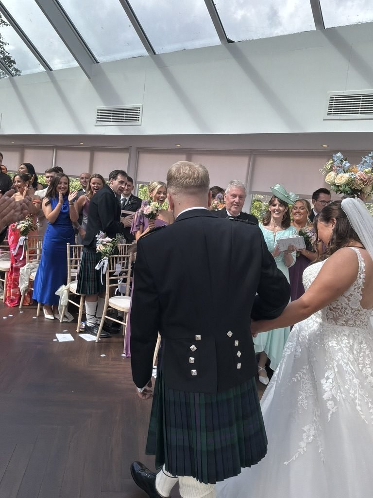 Kyle and Kirsty mid-aisle after being married at Sherbrooke Castle Hotel, guests clapping and holding bouquets on either side