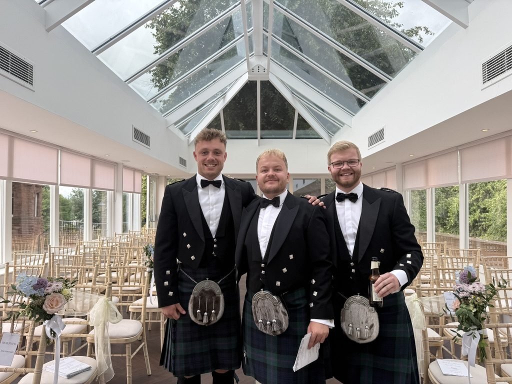 Three groomsmen in black tie and kilts standing together in the Orangery at Sherbrooke Castle Hotel before the wedding