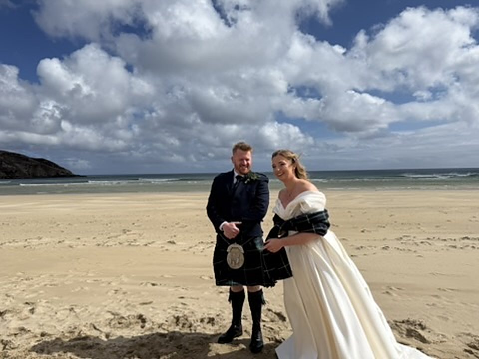 A newly married couple on the white sand of Garry Beach, Isle of Lewis, sea and sky behind them