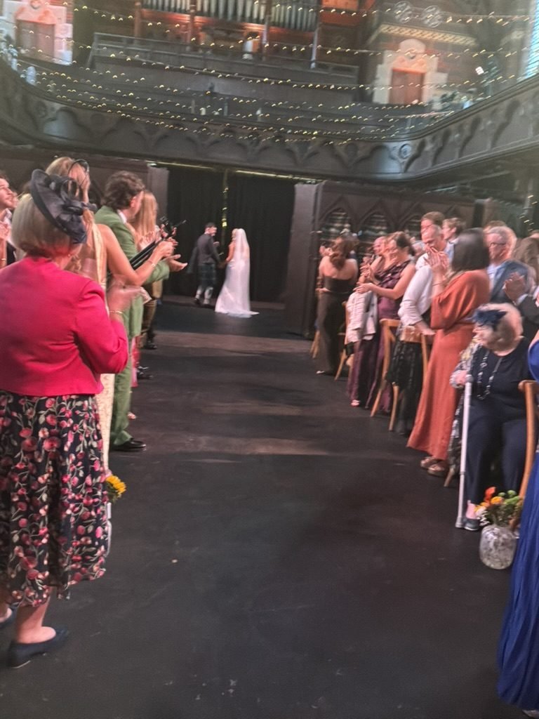 The main hall at Cottiers during the ceremony, fairy lights along the balcony and guests standing either side of the aisle