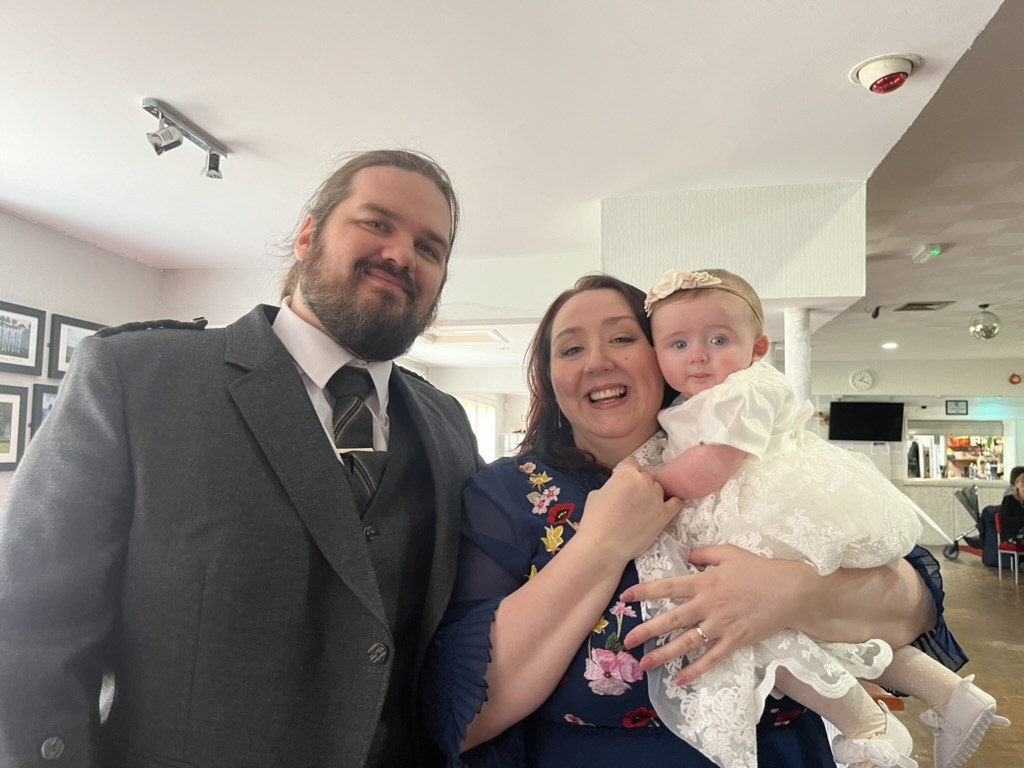 A mum and dad holding their baby daughter in a christening gown at her humanist naming ceremony