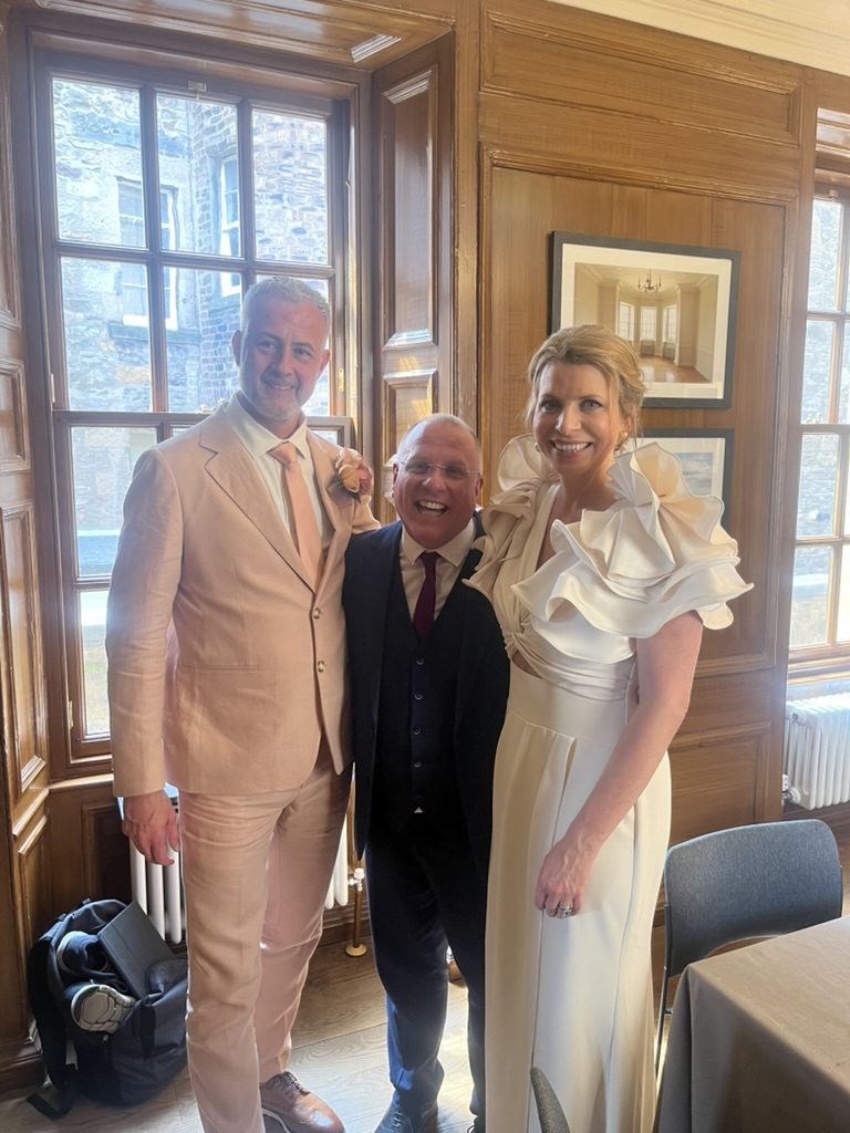 A newly married couple and celebrant John Paul in a wood-panelled room with tall windows at Riddles Court, Edinburgh