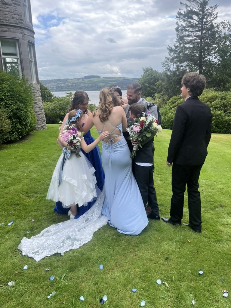 A newly married couple and their family on the lawn at Cats Castle, Cardross, the Firth of Clyde behind