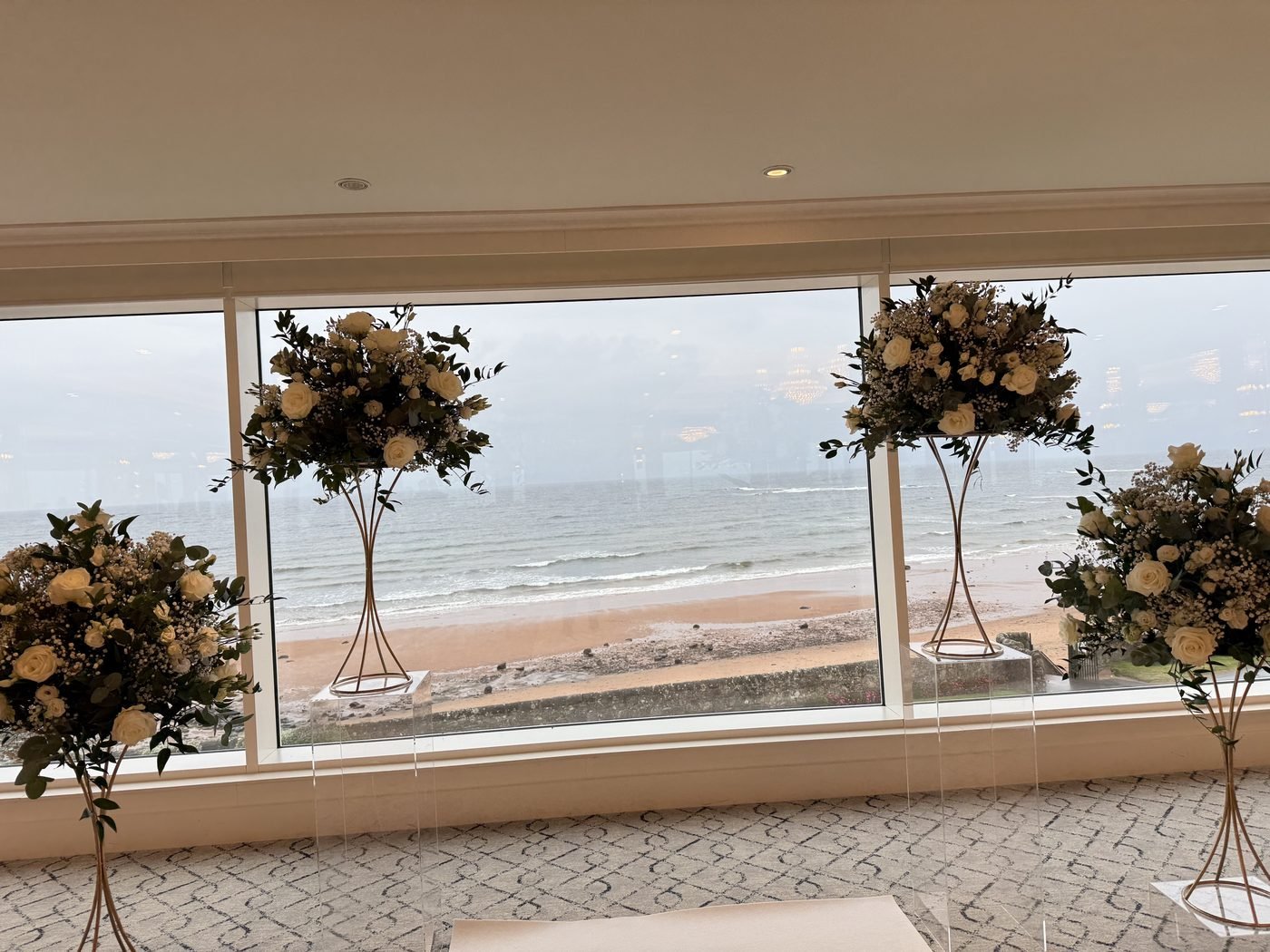 Flower stands framing the Firth Pavilion windows at Seamill Hydro, with the beach and the Firth of Clyde beyond