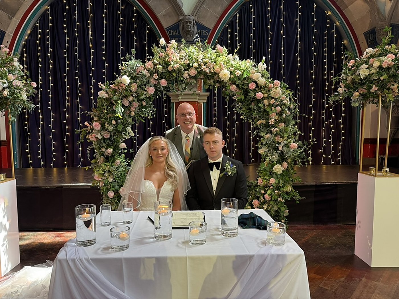 Stuart and Rebecca at the signing table under a flower arch in Òran Mór's Auditorium